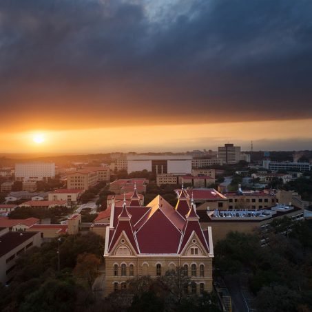 The setting sun blazes through a gap in the heavy clouds behind Old Main and Texas State University.
